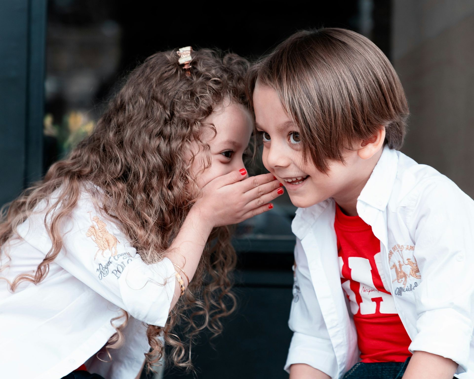 a child with curly hair whispering to another child